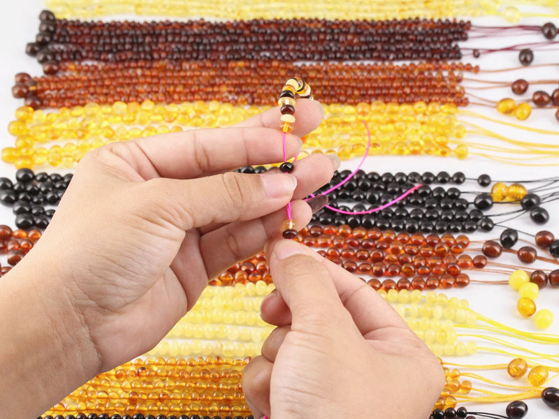 Hand holding a beaded necklace with more beaded necklaces in the background.